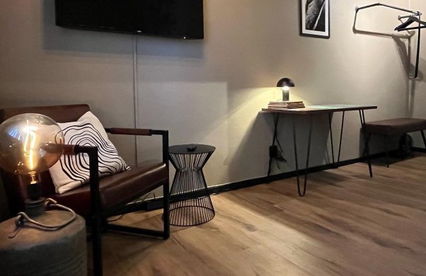 Bild på hotellrum. På bilden syns en fåtölj och två mindre bord; en tv på väggen, ett skrivbord och en klädhängare.