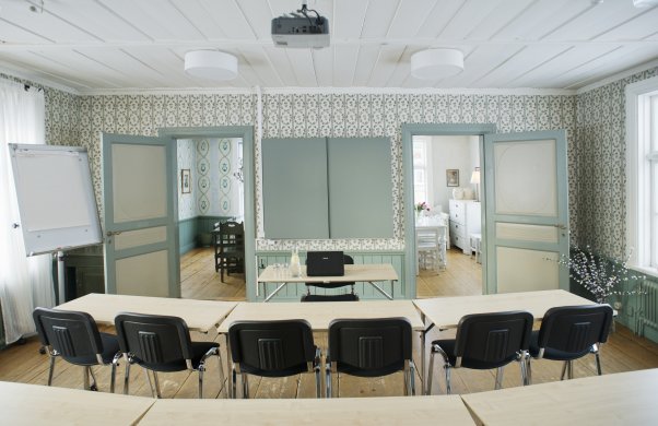 Bild på ett av rummen i konferenslokalen Gammelgård. Rummet är möblerat för möte med bord och stolar på rad.