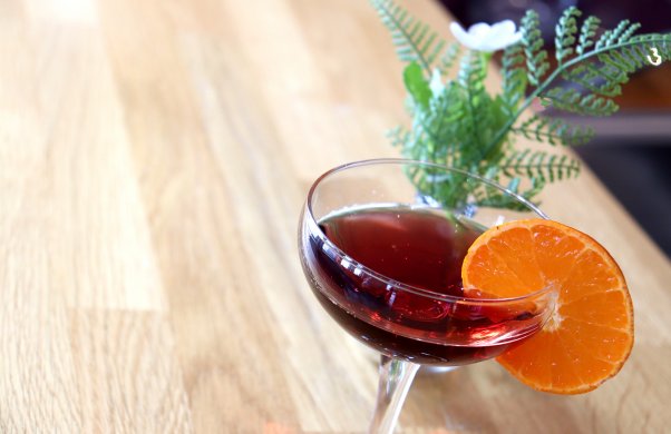 Cocktailglas med röd dryck och en apelsinskiva på glaskanten