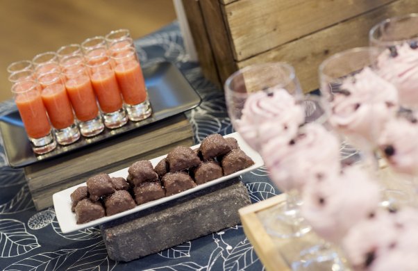 Tre olika efterrätter på ett bord. Längst bort syns små glas med en orange dryck. i mitten en efterrätt av choklad och i förgrunden vinglas med rosa mousse.