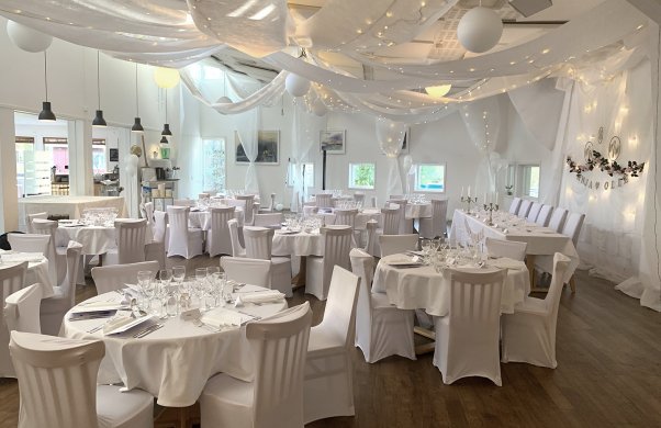 Bröllopsdukning i restaurang Akvarellen. Alla bord och stolar är klädda i vitt tyg. I taket hänger långa vita tyger i böljande former.
