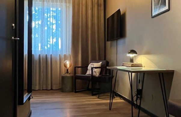 Bild på ett hotellrum. På bilden syns en fåtölj, en tv på väggen och ett skrivnord.