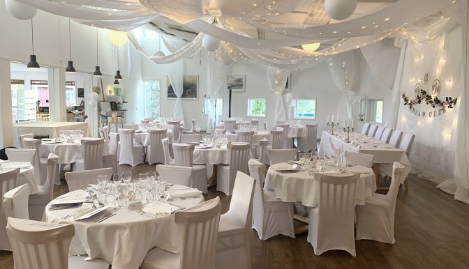 Bröllopsdukning i restaurang Akvarellen. Alla bord och stolar är klädda i vitt tyg. I taket hänger långa vita tyger i böljande former.